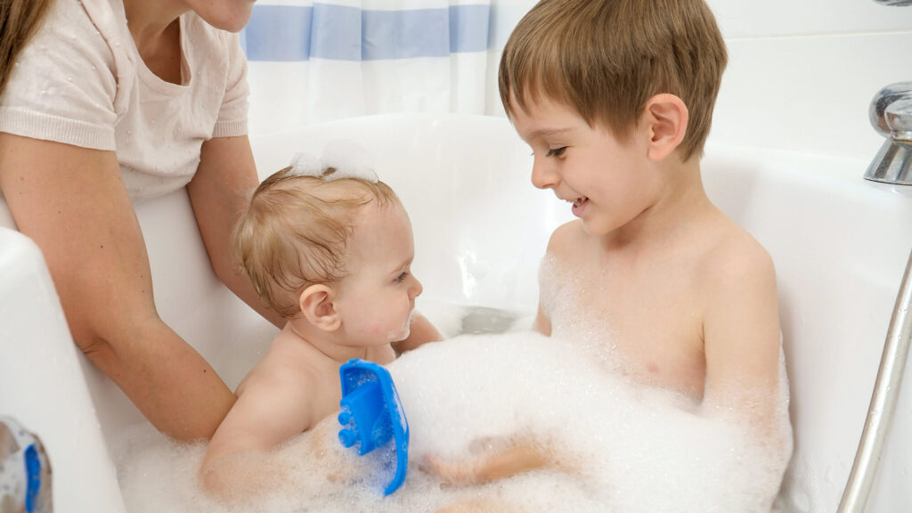 baby boy and older brother washing and playing in hot water bath with foam.